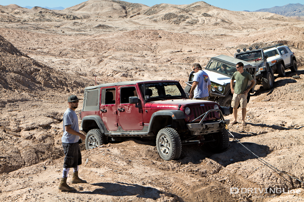 A four-door Jeep Wrangler being towed out of being high-centered with a line of rigs behind it