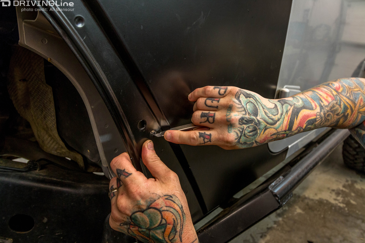 Man cutting a hole in the 3M 1080 Satin Black vehicle wrap that has been installed on a Jeep Wrangler JK