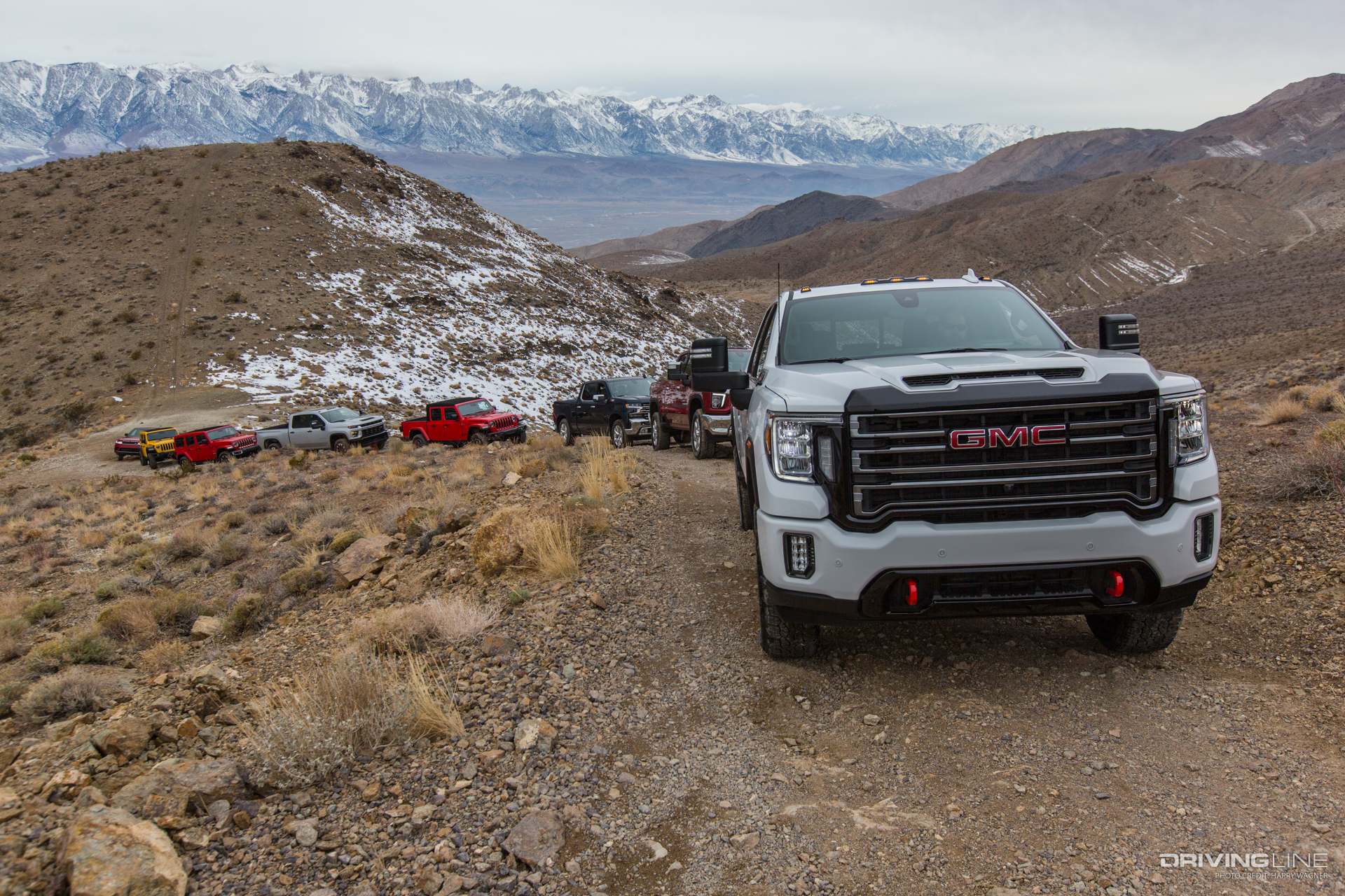 Row of trucks on dirt road with moutains in background